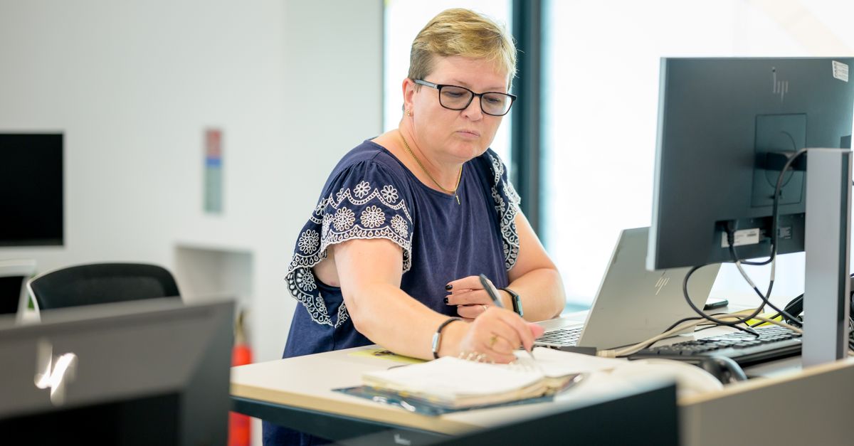 Professional woman wearing eyeglasses working at an office desk with a laptop and notebook.